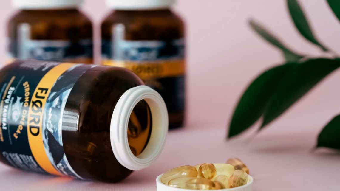 Close-up of omega-3 capsules and bottles on a pink background, ideal for health and wellness themes.