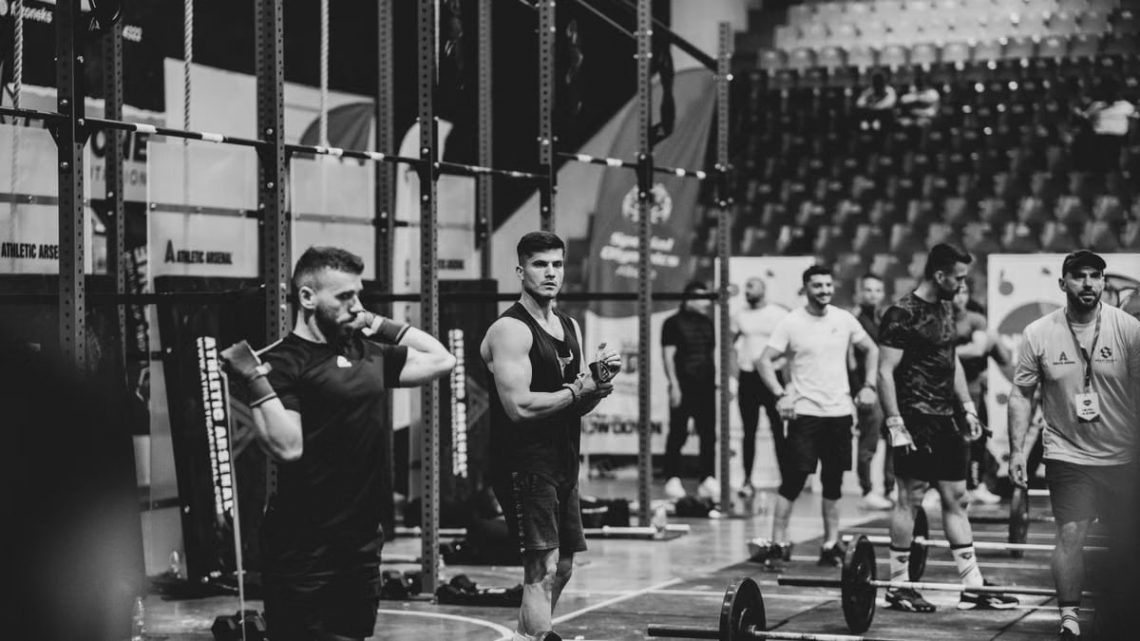Black and white image of a fitness competition showcasing athletes and weights in a gym setting.