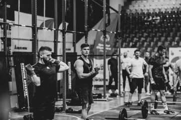 Black and white image of a fitness competition showcasing athletes and weights in a gym setting.